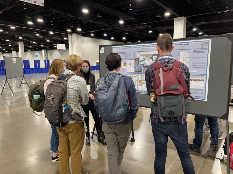 Scientists standing and discussing a poster hanging on a billboard