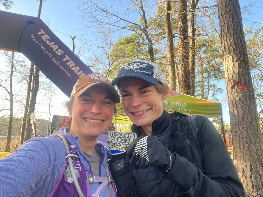 Two women smiling at the finish line of a 100 mile endurance run and holding a finisher's medal.
