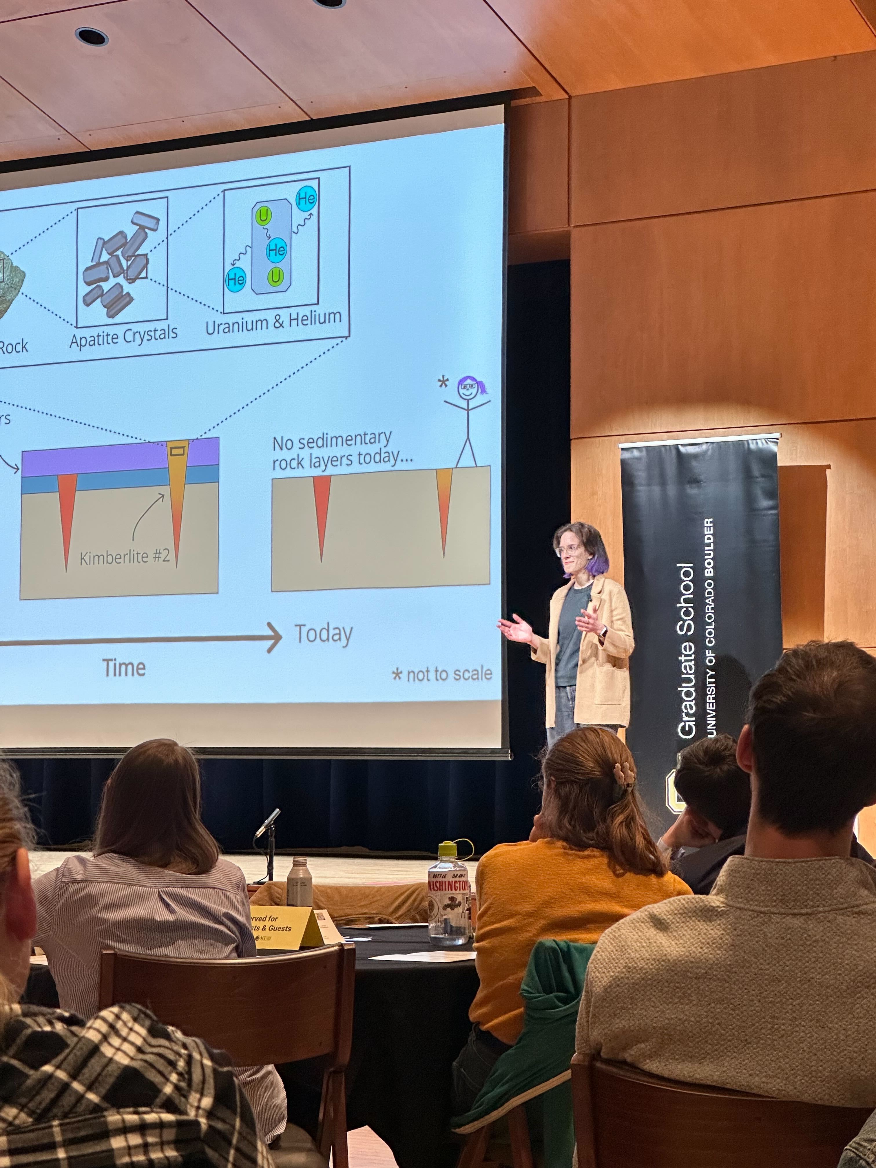 Graduate student standing on stage in front of projected diagram