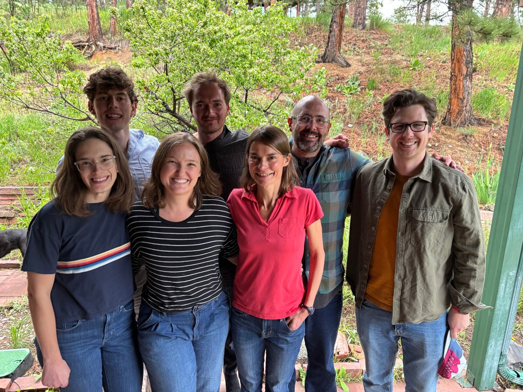 7 geologists smiling at a camera with woods in the background